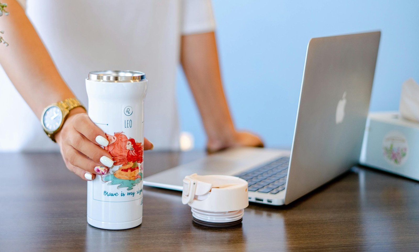 A woman holding an open tumbler next to a macbook