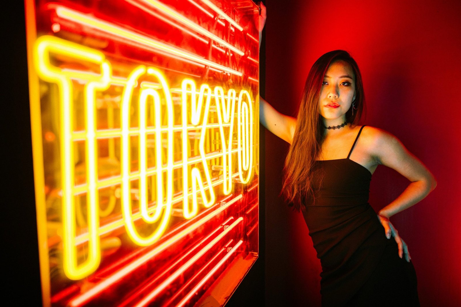 a woman in a black dress standing in front of a neon sign that says Tokyo