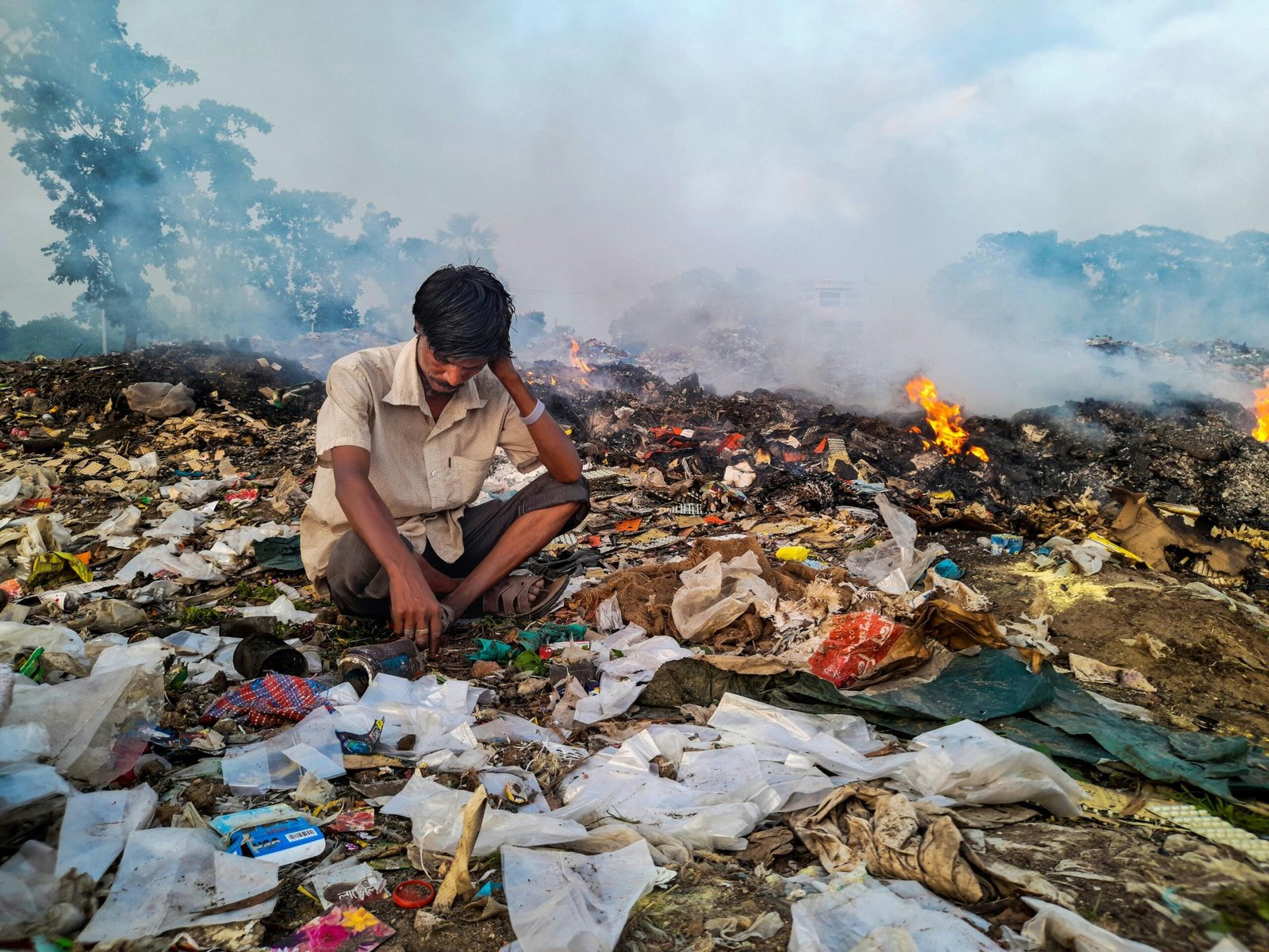 A person sitting on top of garbage while some of them are burning